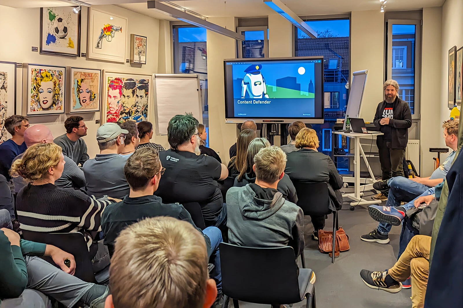 Gruppe von Personen in einem Raum, sitzend und stehend, teilweise mit Computern.